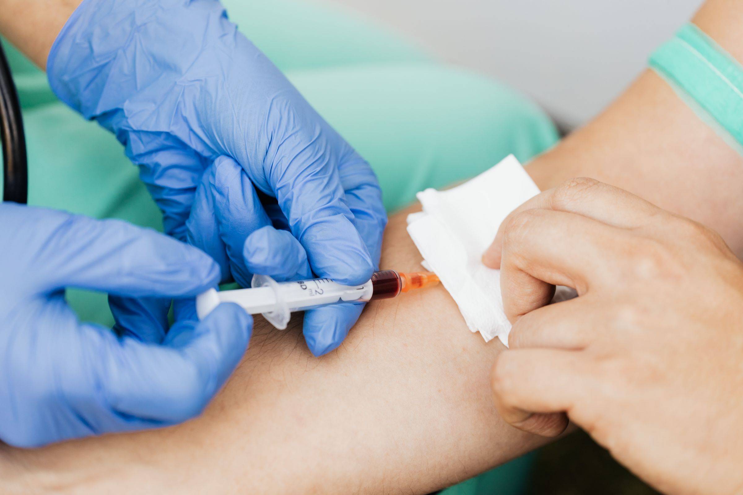 Gloved hands draw blood from a patient’s arm.