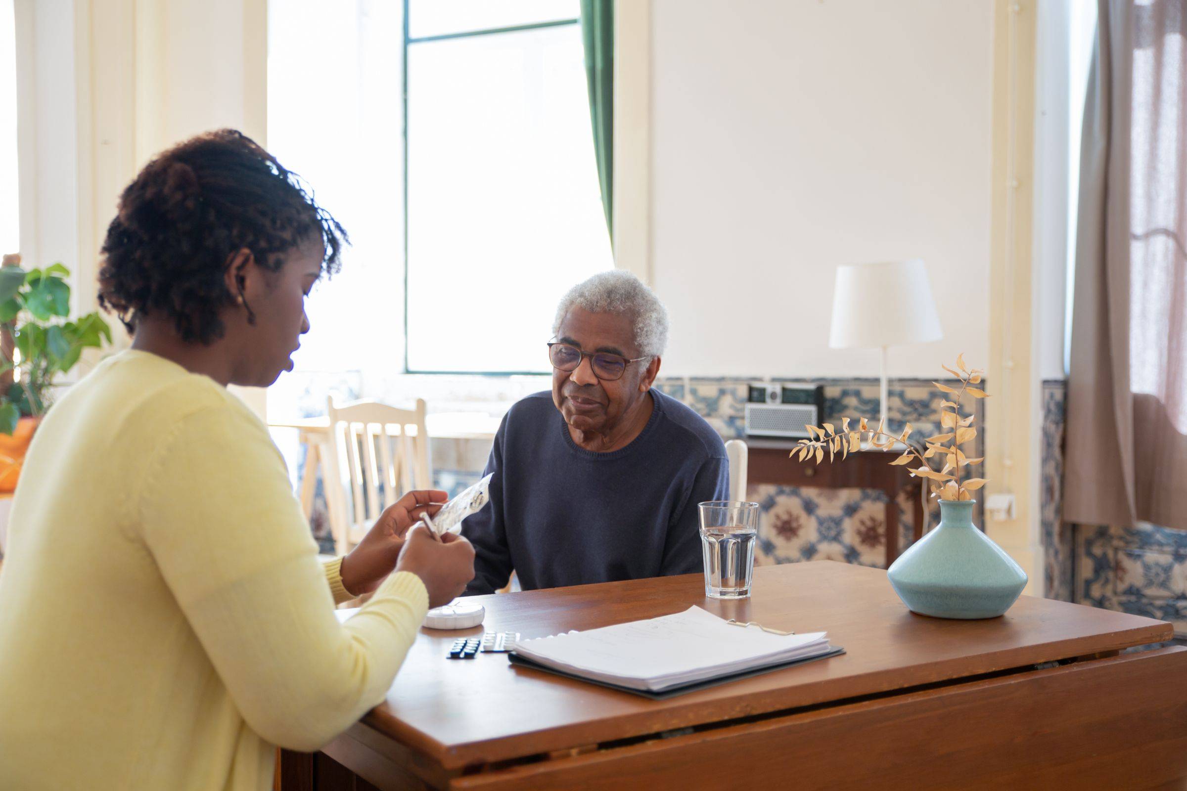 A woman goes through paperwork with an older man at his dining table.